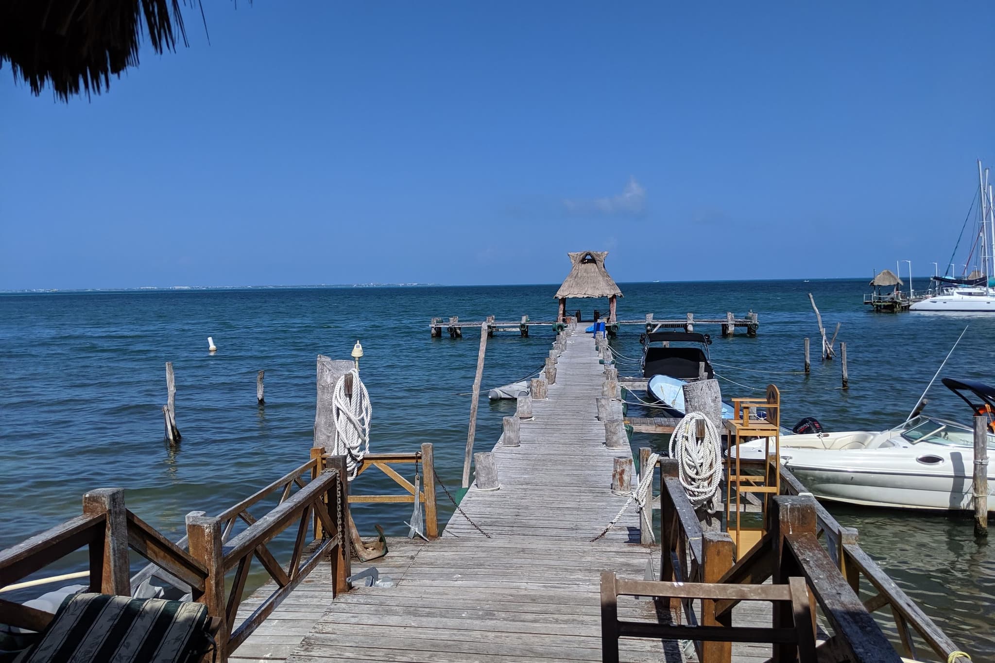 Wooden pier over the sea, with boats moored alongside and a palapa at the end