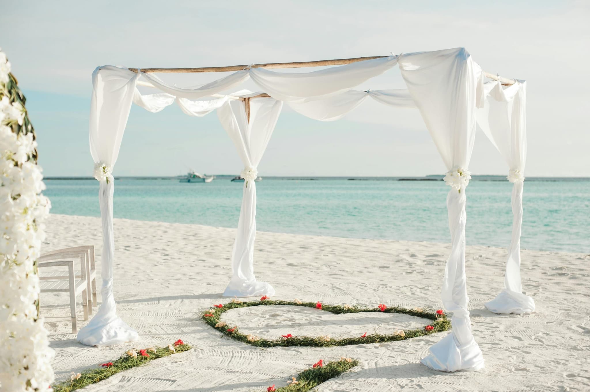 Wedding arch draped in white on the sand, facing the turquoise sea