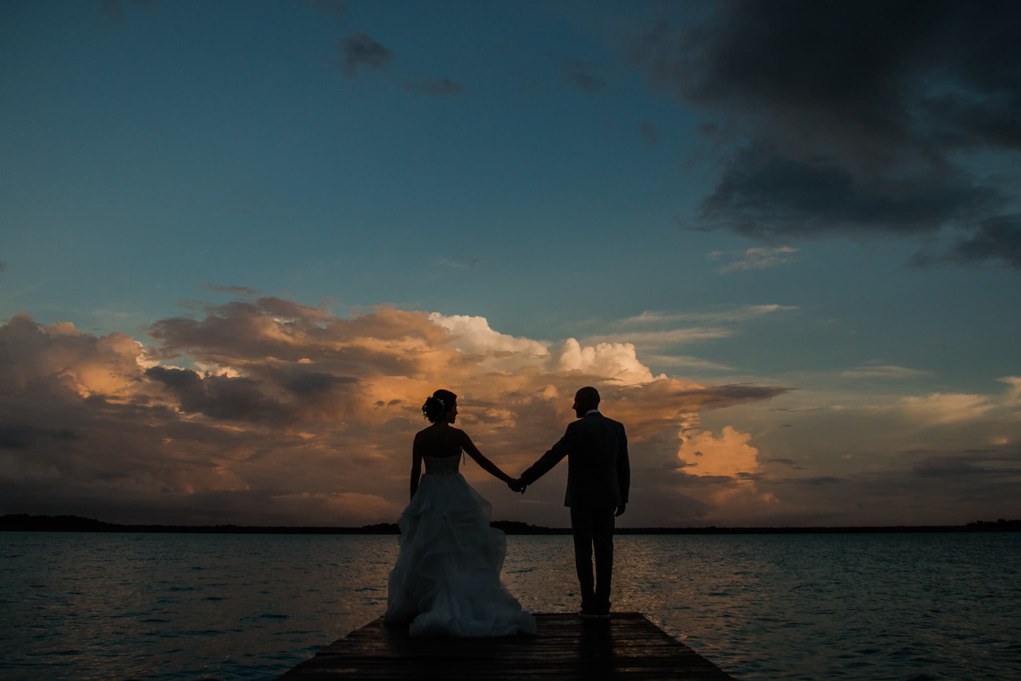 Bride and groom on a dock over the Bacalar lagoon at dusk