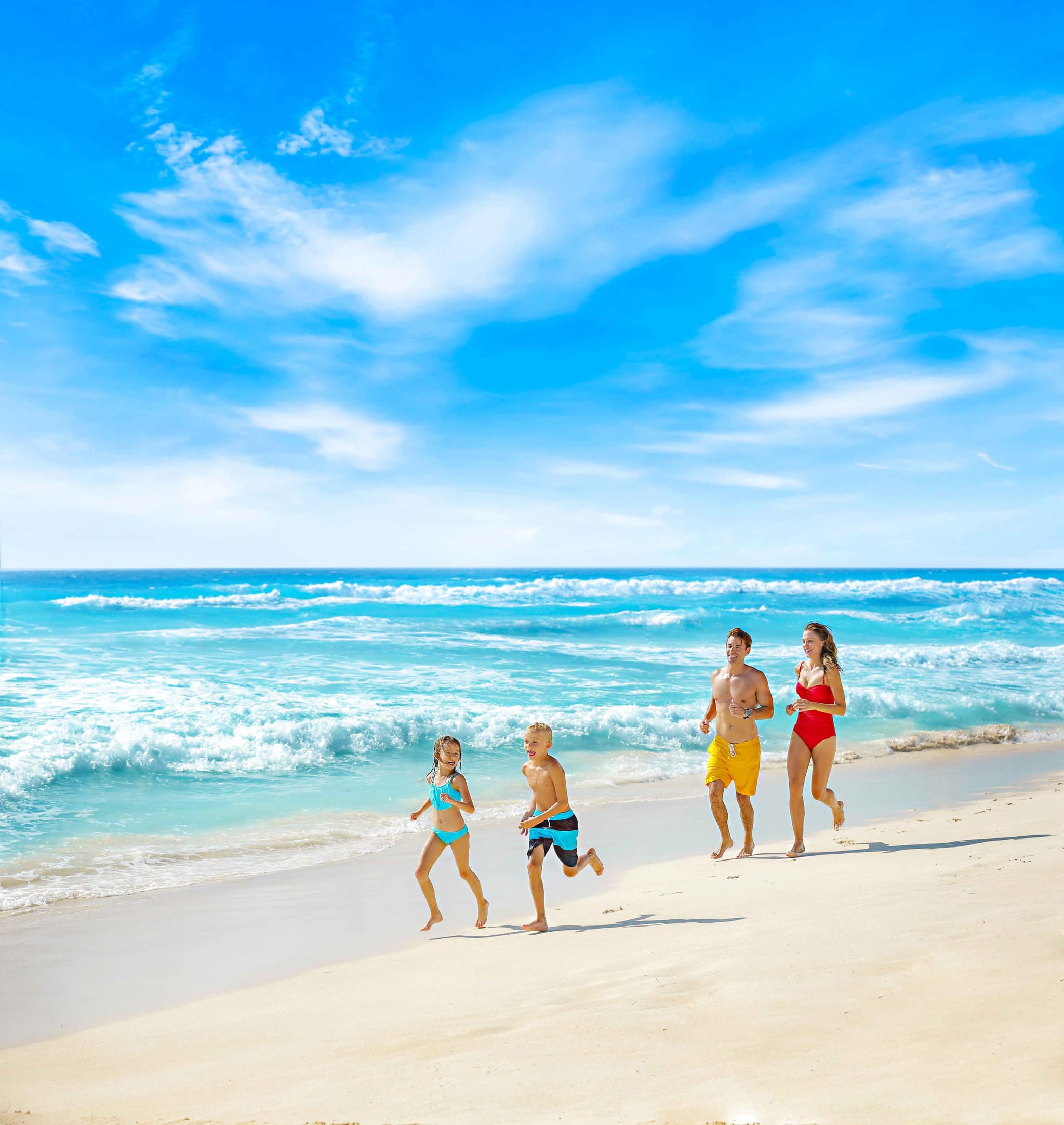 Family running along the shore on a white-sand beach