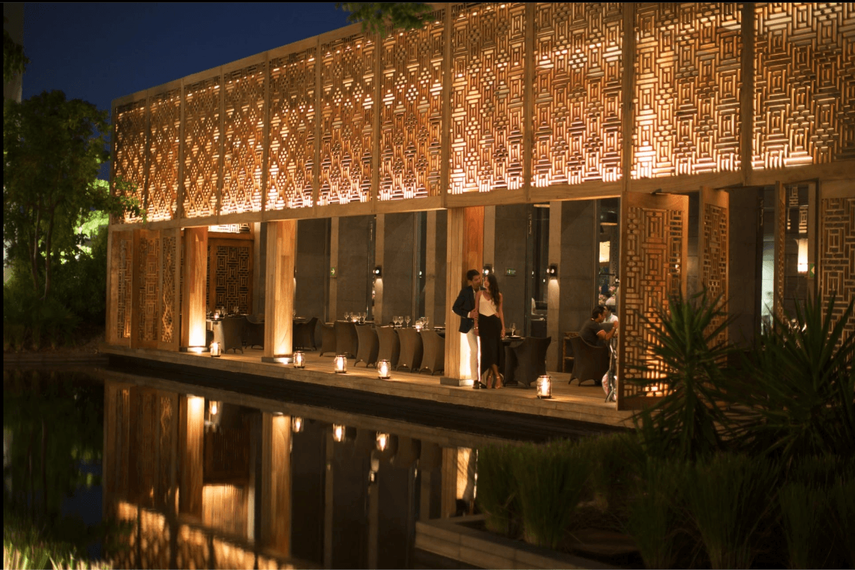 A restaurant lit behind a wooden lattice, reflected in the water