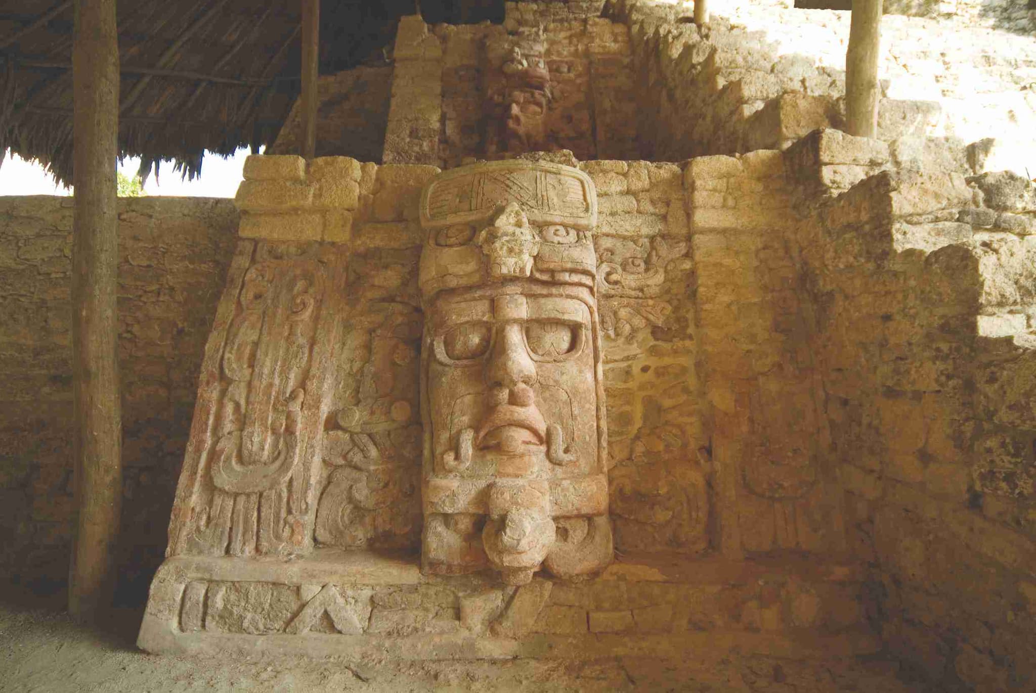 A stucco mask of the sun god at Kohunlich, under its palm roof