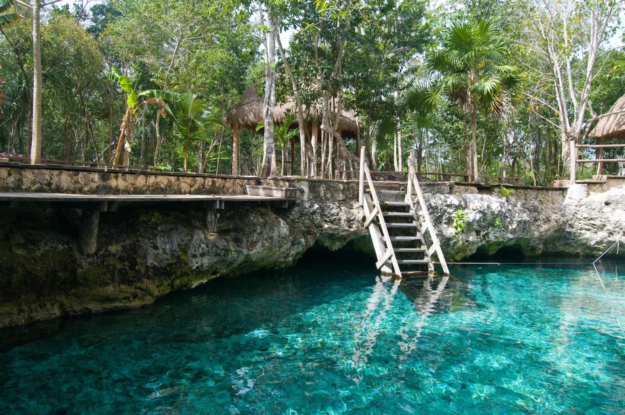 Turquoise cenote with a wooden stairway near Tulum