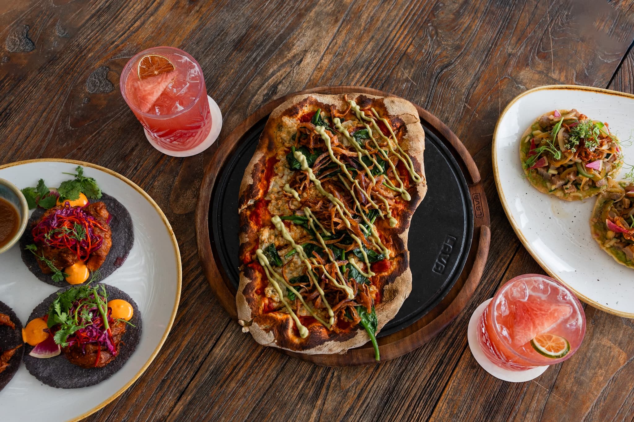 Wood-fired pizza, tostadas and cocktails set out on a wooden table