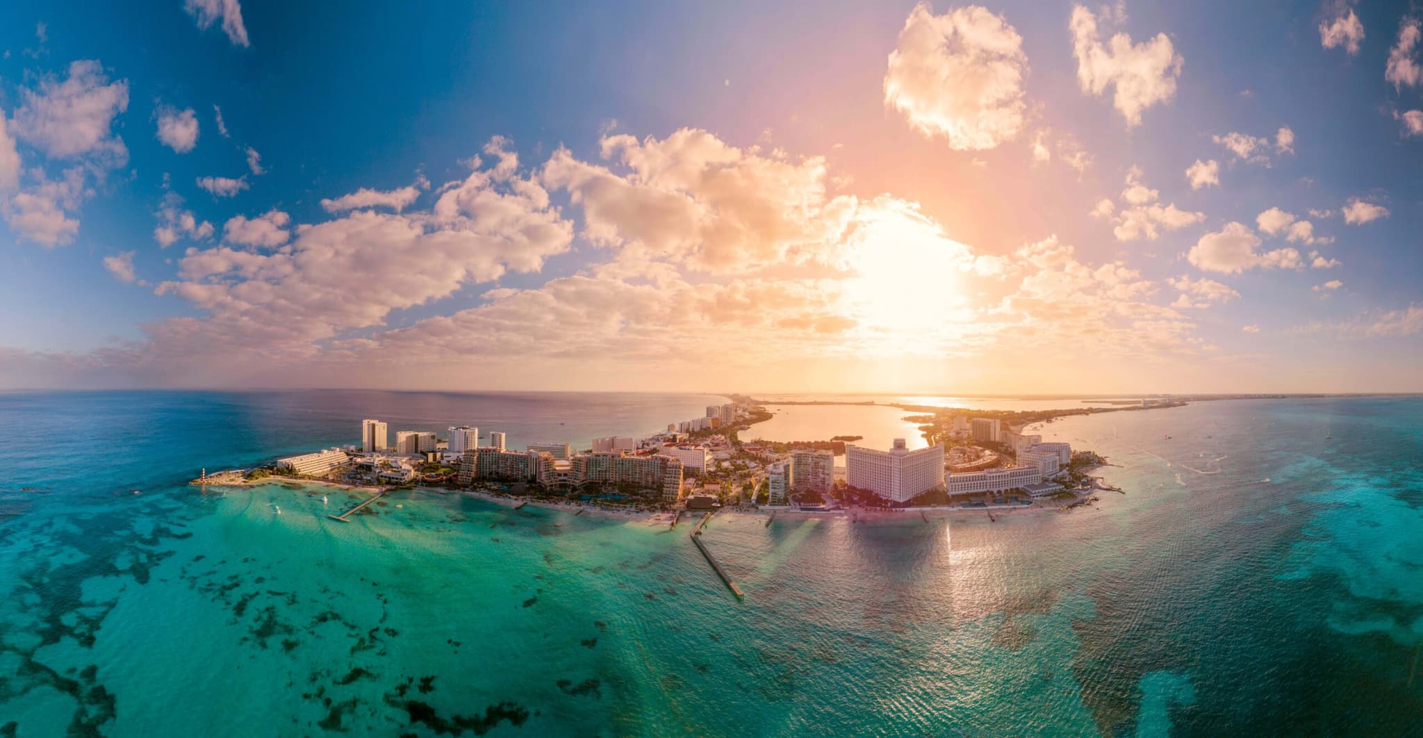 Aerial view of Cancún's Hotel Zone at sunset, with the sun over the sea