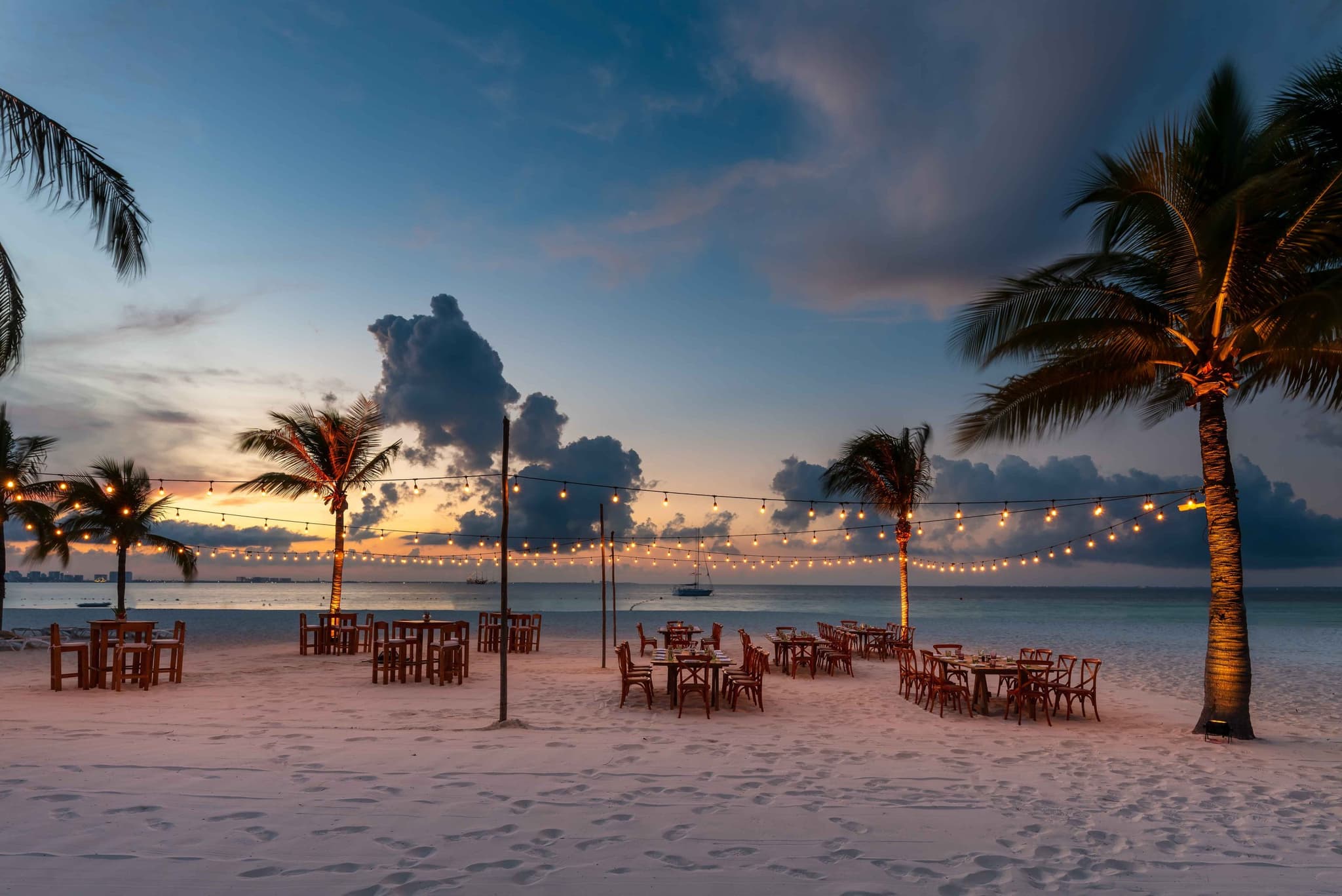 Banquet on the beach under string lights, facing the sea